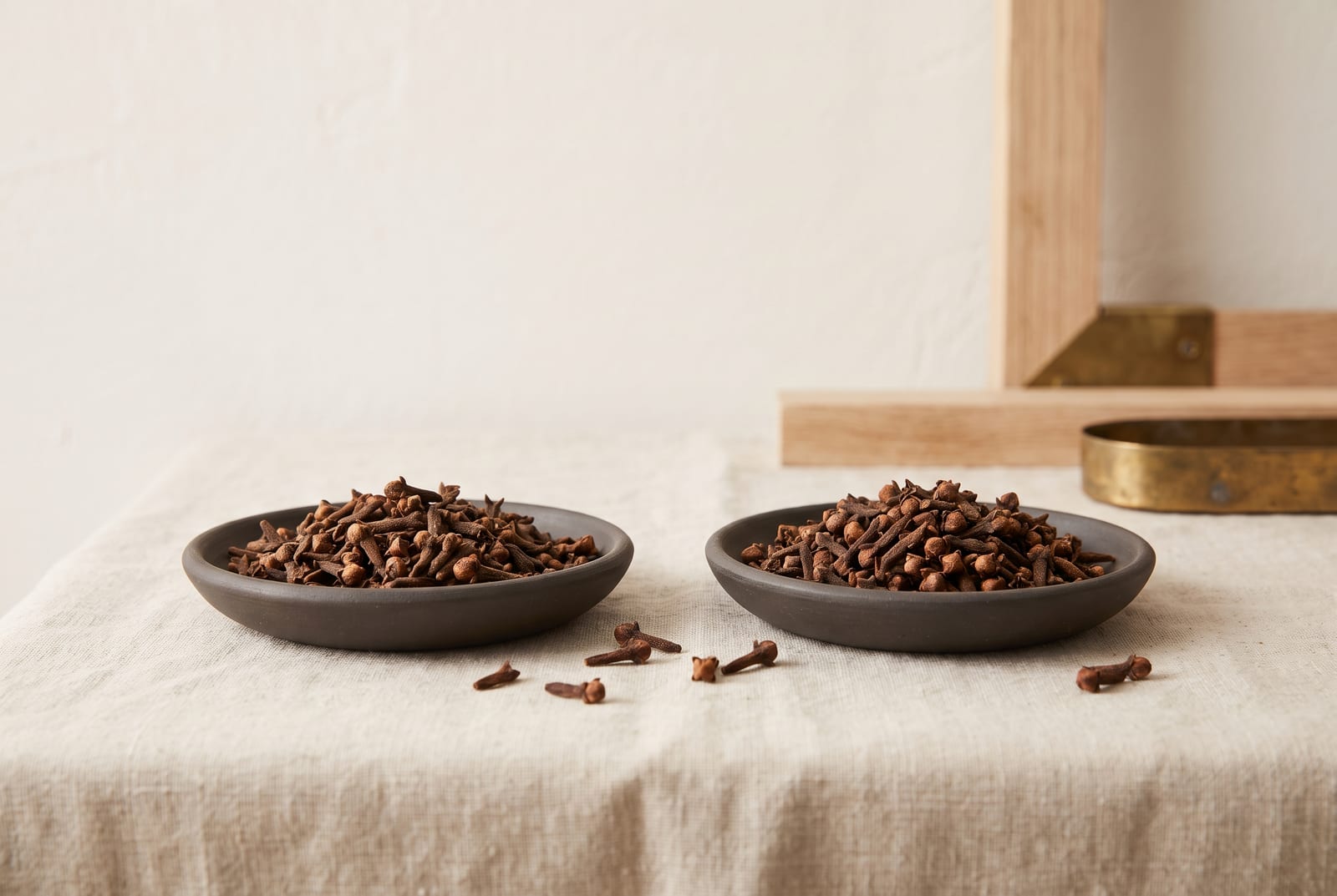 Whole cloves divided evenly between two identical small ceramic dishes on pale linen