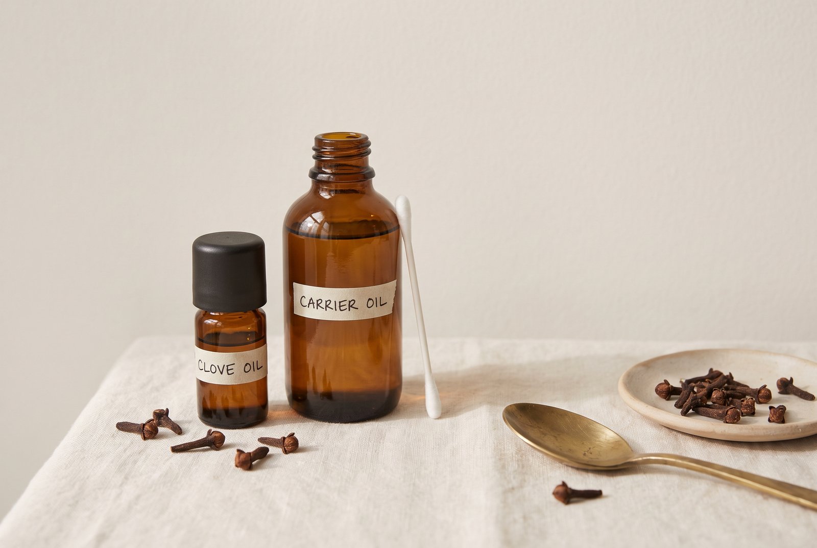 A small bottle of clove oil beside a carrier oil and a cotton swab