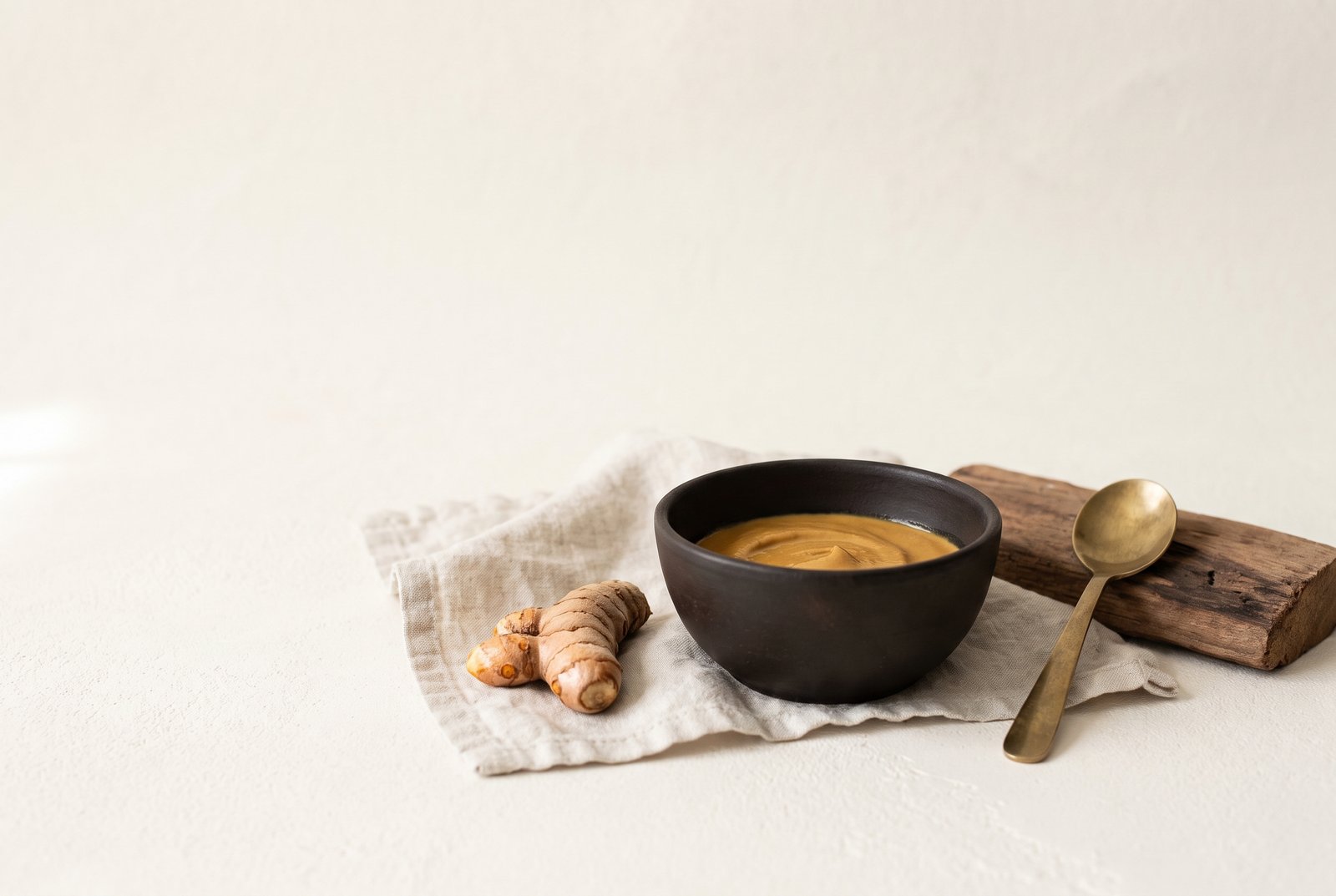 A turmeric skincare mask in a bowl beside fresh turmeric root
